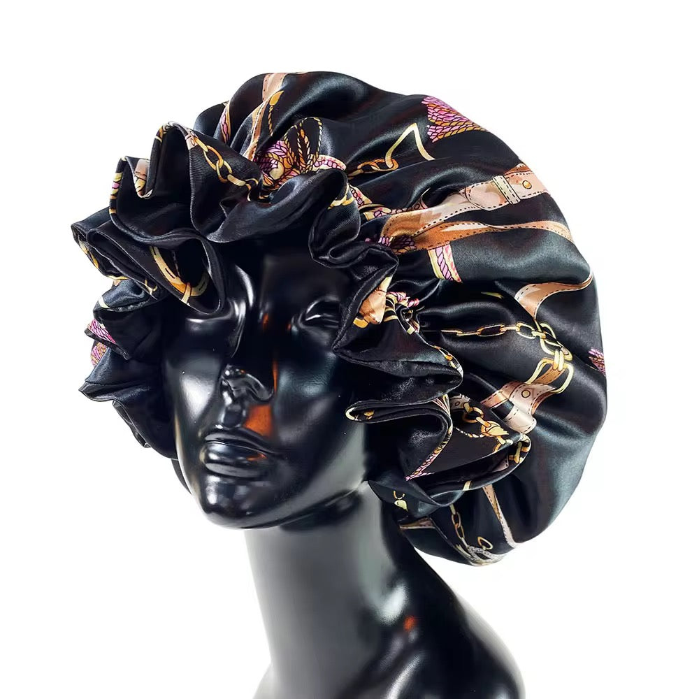 Black satin bonnet with gold and pink patterns on a mannequin head against a white background