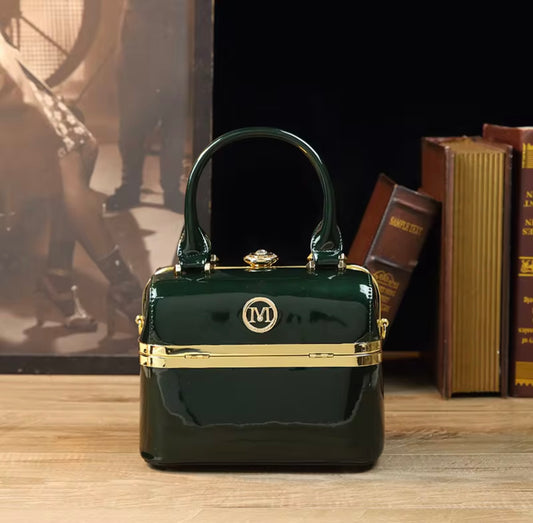 Green handbag with gold accents on a wooden surface with books and a horse painting in the background